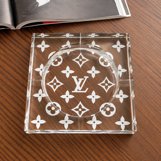 Large square crystal glass ashtray with etched monogram-flower pattern on wooden coffee table, top view